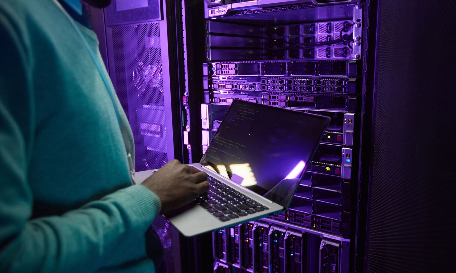 Cropped shot of African American data engineer holding laptop while working with supercomputer in server room lit by blue light, copy space
